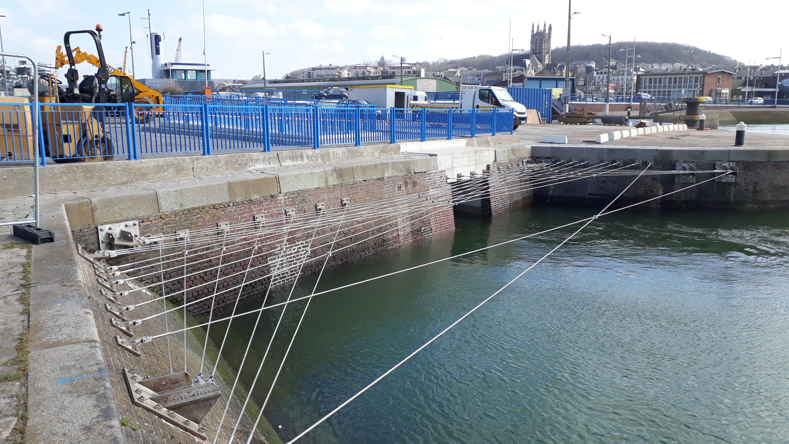 Vue d'un bassin portuaire avec un dispositif de filins accrochés aux murs au-dessus de l'eau pour empêcher le braconnage par le pêche.